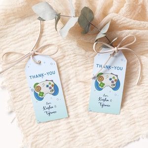 May include: Two blue and white thank you tags with a cartoon video game controller. The text on the tags reads "Thank You" and "Love Keisha & Tyrone".