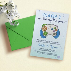 May include: A blue and white baby shower invitation with a cartoon video game controller. The invitation reads "Player 3 is entering the game!" and includes the names "Keisha & Tyrone", the date and time of the shower, and the address.