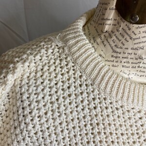 May include: A cream-colored knitted sweater with a loose, open weave. The sweater is on a mannequin and has a crew neck.
