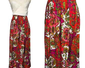 May include: A vintage, floor-length skirt with a vibrant paisley pattern in red, pink, green, and white. The skirt has a high waist and a flowing silhouette. The fabric appears to be lightweight, suitable for warmer weather. The skirt is paired with a white top.
