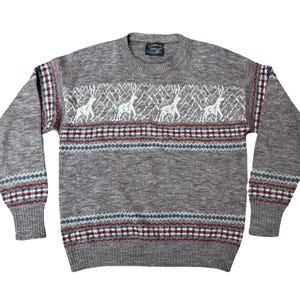May include: A gray sweater with a crew neck and long sleeves. The sweater features a pattern of white deer and geometric designs in red, white, and blue. The cuffs and hem are ribbed.