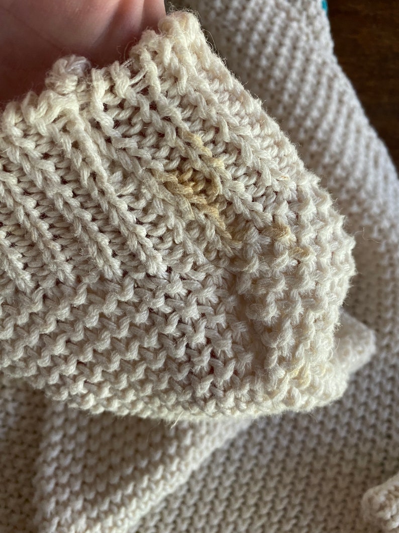 May include: Close-up of a cream-colored knitted sweater with a small yellow stain.
