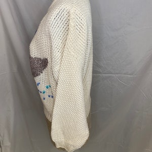 May include: White knitted sweater with a colorful geometric design. The sweater has a crew neck and long sleeves.