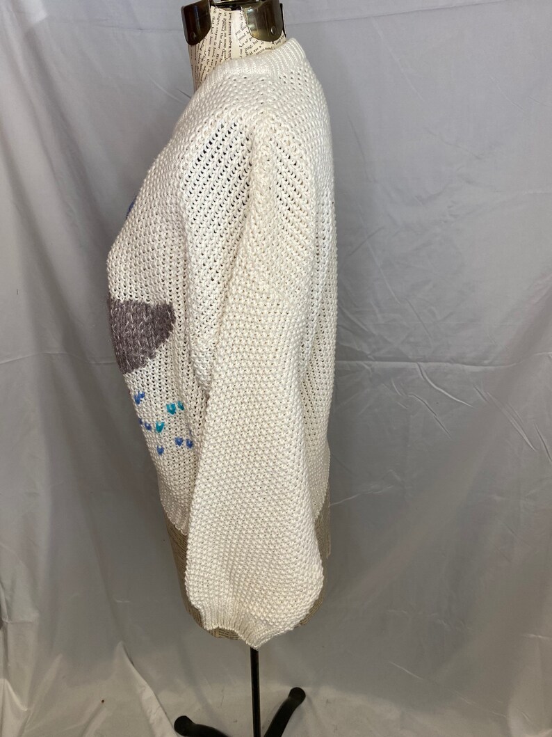 May include: White knitted sweater with a colorful geometric design. The sweater has a crew neck and long sleeves.
