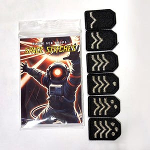 Könnte beinhalten: Sechs schwarze, bestickte Rangabzeichen mit silbernen Chevron-Mustern, vertikal angeordnet, neben einer durchsichtigen Plastiktüte mit einer Karte, die eine Astronauten-Illustration und den Text Black Sea Props Space Stitches zeigt.