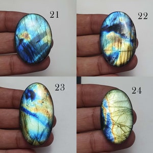 May include: Four oval-shaped labradorite gemstones with iridescent blue, green, and gold colors. The stones are labeled 21, 22, 23, and 24.