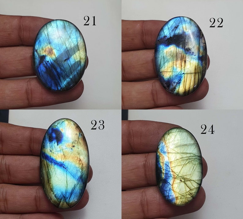 May include: Four oval-shaped labradorite gemstones with iridescent blue, green, and gold colors. The stones are labeled 21, 22, 23, and 24.