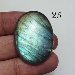 May include: A green and blue oval-shaped labradorite gemstone with a iridescent sheen. The gemstone is approximately 25 mm in size.