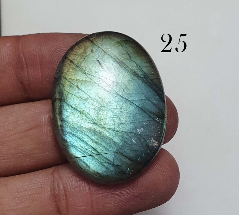 May include: A green and blue oval-shaped labradorite gemstone with a iridescent sheen. The gemstone is approximately 25 mm in size.
