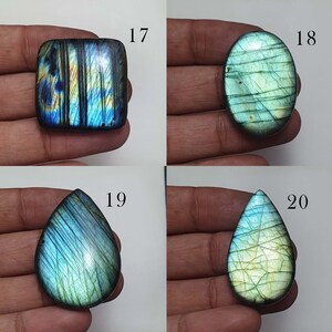 May include: Four labradorite gemstone cabochons in various shapes and sizes. The cabochons are a mix of blue, green, and gold colors with iridescent shimmer. The cabochons are labeled with numbers 17, 18, 19, and 20.