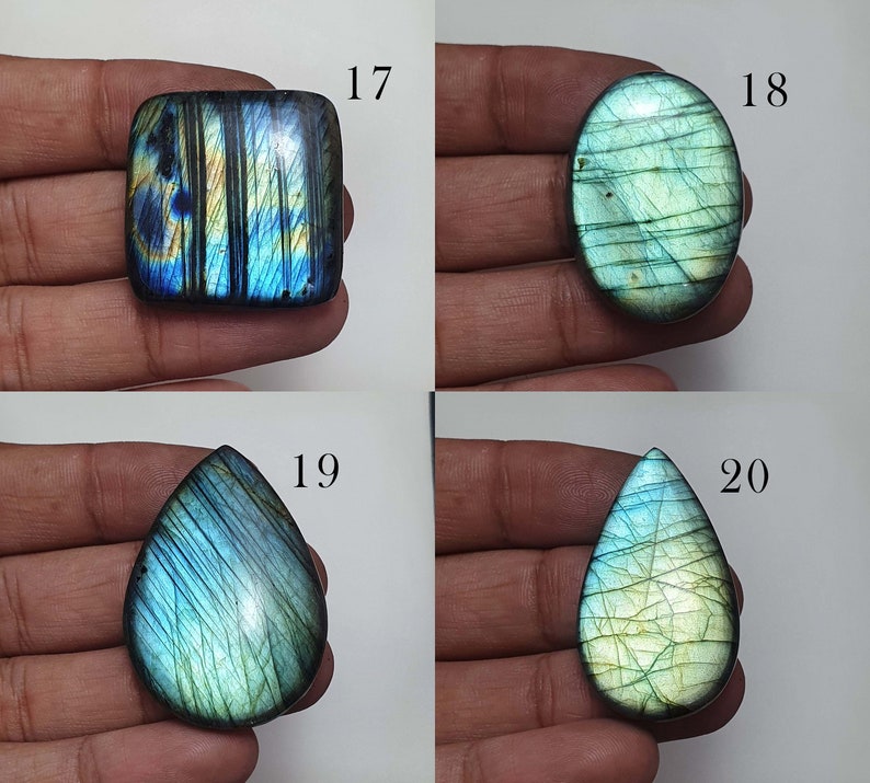 May include: Four labradorite gemstone cabochons in various shapes and sizes. The cabochons are a mix of blue, green, and gold colors with iridescent shimmer. The cabochons are labeled with numbers 17, 18, 19, and 20.