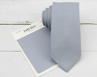 May include: A dusty blue necktie paired with a matching fabric swatch on a white card. The card features the text David's Bridal and the color name Dusty Blue. The necktie has a smooth, solid-colored finish and a pointed tip.