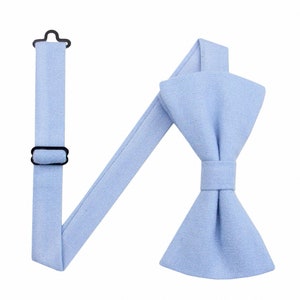 May include: A light blue bow tie with adjustable straps. The bow tie is made of a textured fabric.
