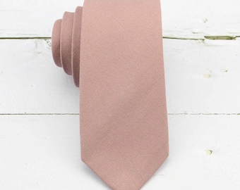 May include: A solid dusty rose necktie with a matte, textured fabric finish. The necktie is rolled at the top and features a pointed tip at the bottom, displaying a consistent, uniform color throughout the entire length of the accessory.