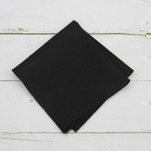 May include: A black square pocket square, folded and lying flat on a white wooden surface.