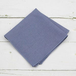 Puede incluir: Un pañuelo de bolsillo azul sólido hecho de tela de algodón. El cuadrado está doblado por la mitad y tiene una textura lisa y uniforme.