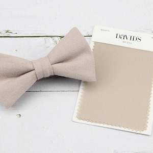 Puede incluir: Una pajarita beige claro hecha de tela, junto a una muestra de tela etiquetada "David's Bridal" en beige.