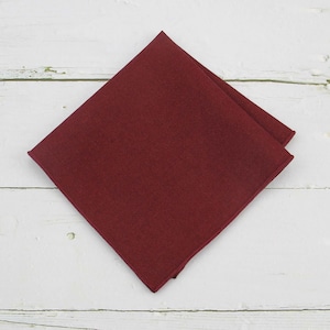 May include: A solid burgundy red pocket square. The square is made of a smooth, soft fabric.