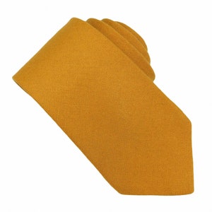 May include: A solid mustard yellow necktie with a textured fabric finish. The tie is folded over itself, showing the pointed end and the smooth, consistent weave of the material against a plain white background for clear visibility.