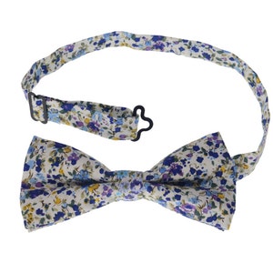 May include: A white bow tie with a blue and purple floral pattern. The bow tie has an adjustable strap with a metal clasp.