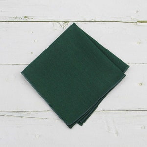 May include: A square pocket square in a solid dark forest green color. The fabric features a smooth, uniform texture with clean, stitched edges, folded into a diamond shape to display its deep, saturated hue and consistent finish.