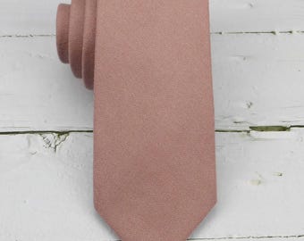 May include: A solid dusty rose necktie with a textured fabric finish, rolled at the top and tapering to a pointed end at the bottom. The necktie features a consistent matte color throughout its length, showcasing a woven material appearance.