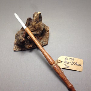 以下が含まれることがあります： 銀色の先端を持つ木の杖が、流木の上に置かれています。杖には「No. 205 Point D'Argent オーク」とラベルが貼られています。
