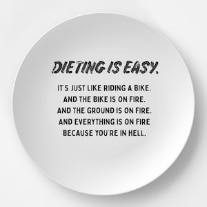 May include: White ceramic plate with black text that reads "DIETING IS EASY. IT'S JUST LIKE RIDING A BIKE. AND THE BIKE IS ON FIRE. AND THE GROUND IS ON FIRE. AND EVERYTHING IS ON FIRE BECAUSE YOU'RE IN HELL."