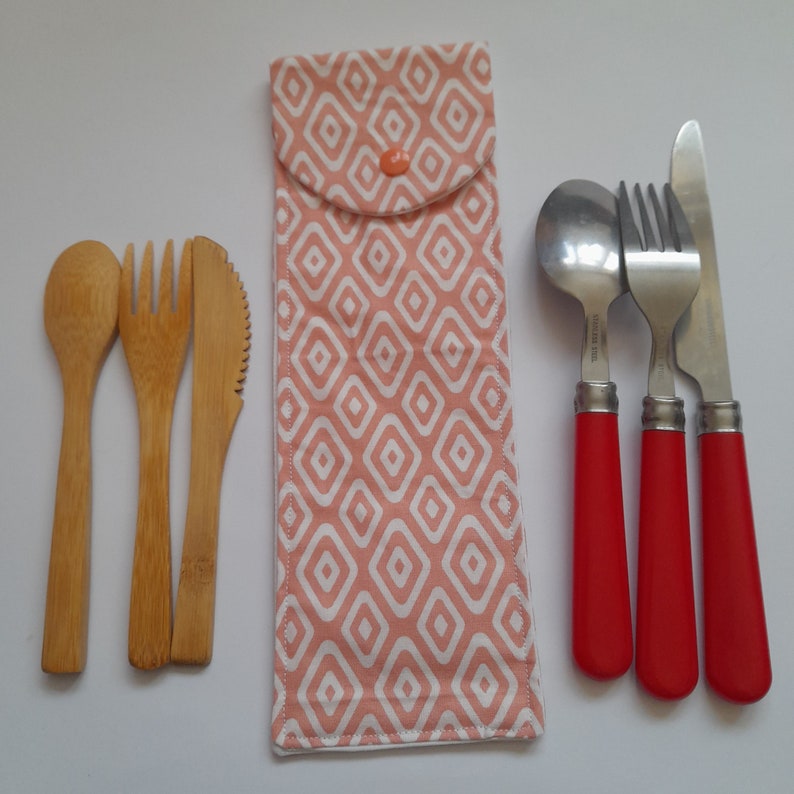May include: A set of reusable cutlery in a pink and white patterned fabric pouch. The set includes a wooden spoon, fork, and knife, and a metal spoon, fork, and knife with red handles.