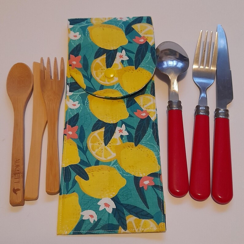 May include: A set of reusable cutlery in a lemon print fabric pouch. The set includes a fork, knife, spoon, and two wooden chopsticks. The cutlery has red handles.