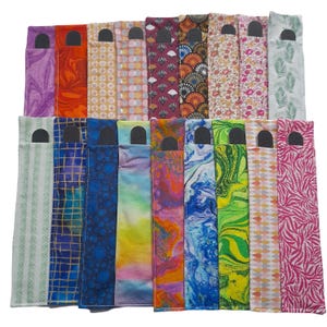May include: A selection of patterned pen cases in various colours. The cases display diverse designs, such as floral, geometric, and abstract patterns. Each case has a black top with a rectangular opening. The cases are arranged in rows, showcasing the variety of designs.