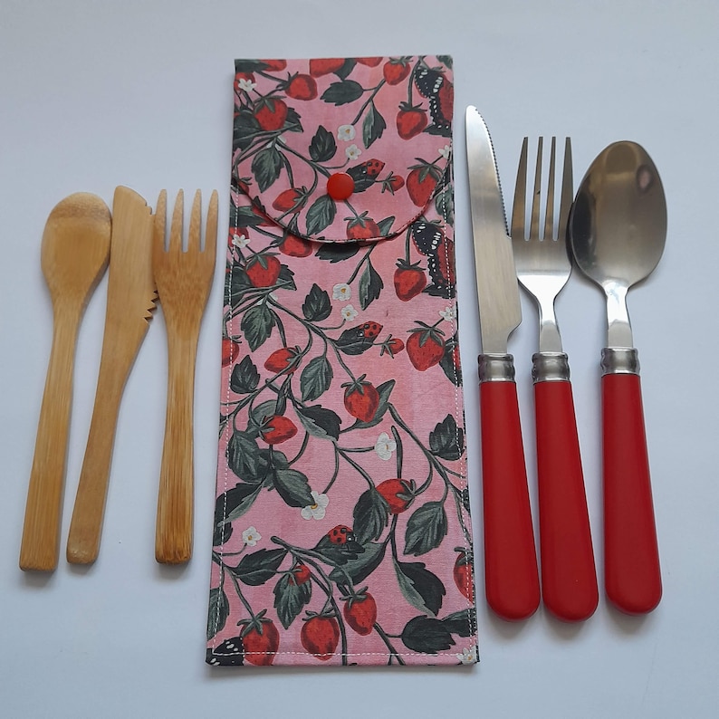 May include: A set of reusable cutlery with a pink and green strawberry print carrying case. The set includes a fork, knife, spoon, and two wooden utensils.