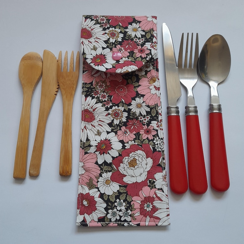 May include: A set of reusable cutlery with a floral print carrying case. The set includes a knife, fork, spoon, and two wooden utensils. The cutlery has red handles and the case has a pink and white floral pattern.