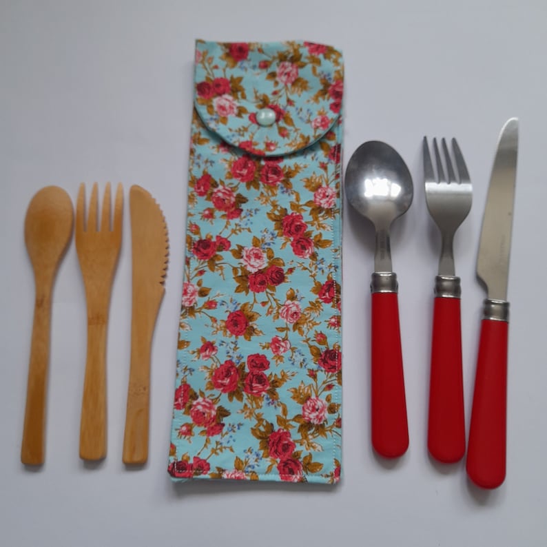 May include: A set of cutlery with a floral patterned fabric case. The set includes a spoon, fork, and knife. The cutlery is made of metal with red handles. The case is blue with pink and white flowers.