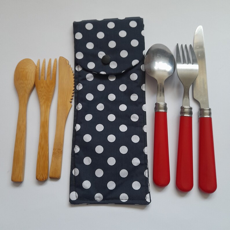 May include: A set of cutlery with a black and white polka dot carrying case. The set includes a wooden spoon, two wooden forks, a wooden knife, a spoon with a red handle, a fork with a red handle, and a knife with a red handle.