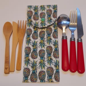 May include: A set of reusable cutlery in a pineapple patterned fabric pouch. The set includes a spoon, fork, knife, and a small wooden knife. The cutlery is made of stainless steel and has red handles. The pouch is made of cotton and has a zipper closure.