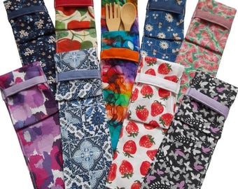 May include: A collection of reusable utensil pouches in various patterns. Designs include floral, fruit, and abstract prints. One pouch contains a wooden fork and spoon. Each pouch has a coordinating fabric closure.