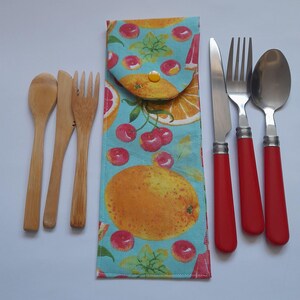 May include: A set of reusable cutlery with a colorful fabric case. The cutlery includes a knife, fork, spoon, and two wooden chopsticks. The case has a blue background with a pattern of oranges, cherries, and leaves.