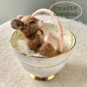 May include: A handcrafted felt mouse with brown and white fur, nestled in a white teacup with a gold rim and blue polka dots. The mouse has a pink tail and is lying on a bed of white fluff. Text in a speech bubble reads, "I'm a PDF download."