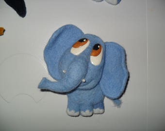 May include: A blue plush elephant toy with large brown eyes and a long trunk. The elephant is sitting on a white surface.