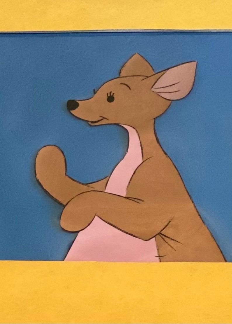 Puede incluir: Un canguro de dibujos animados marr&oacute;n con detalles rosas y orejas grandes, de pie sobre un fondo azul.