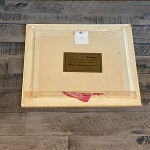 Puede incluir: Un marco blanco con un passe-partout y una etiqueta dorada que dice "This is an Original Hand Painted Celluloid Drawing Actually Used in a Walt Disney Production".