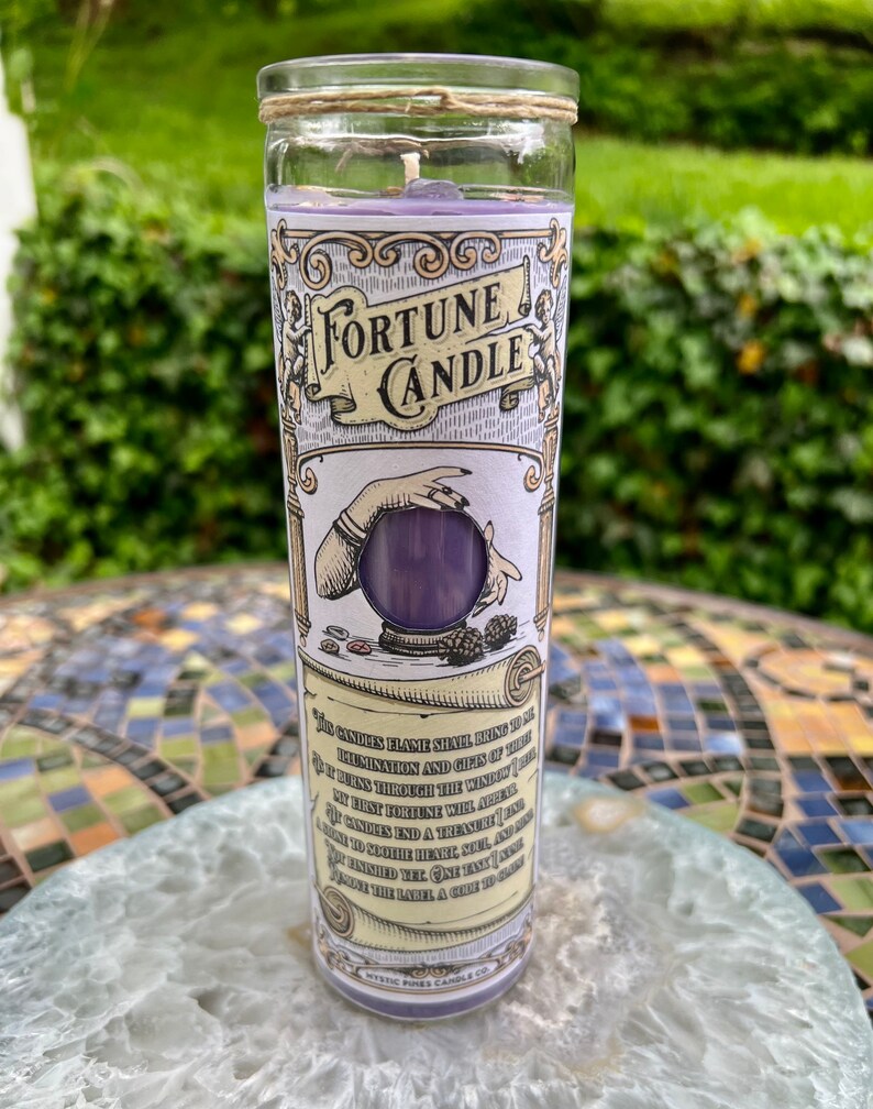 May include: A purple fortune candle in a glass jar with a twine lid. The label features a hand holding a crystal ball and the text "Fortune Candle". The text on the label reads "This candle's flame shall bring to thee illumination and gifts of the..."