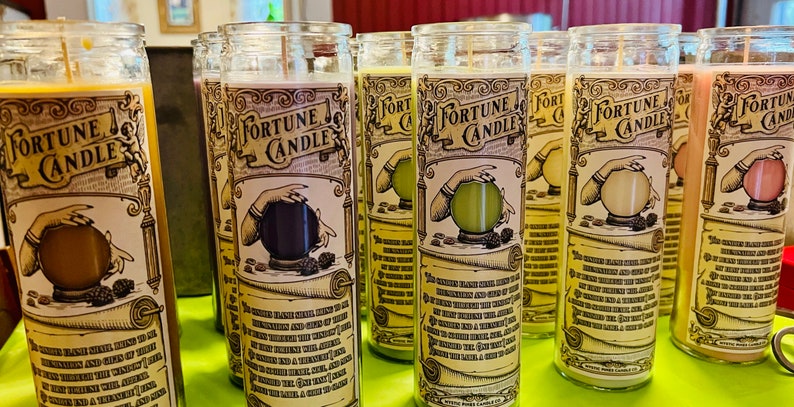 May include: A set of six glass fortune candles with a vintage design. Each candle features a hand holding a crystal ball with a different color inside. The candles are labeled "Fortune Candle" and have a text description on the side.