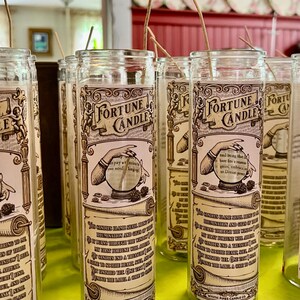 May include: A row of clear glass fortune candles with a vintage design. Each candle features a hand holding a crystal ball and the text "Fortune Candle".