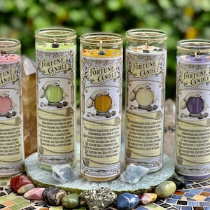 May include: Four fortune candles with different colored wax and crystals inside. Each candle has a label that says "Fortune Candle" and features a hand holding a crystal ball. The labels also include a description of the candle's purpose.