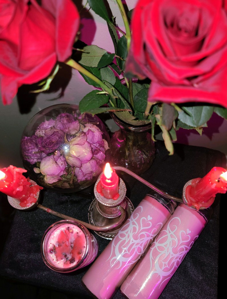 May include: Two pink candles with white designs and a heart motif, two red candles in silver candle holders, and a glass bowl filled with dried pink roses.