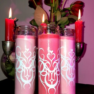 May include: Three pink and red glass candles with white decorative designs. The candles are in glass holders and are lit.