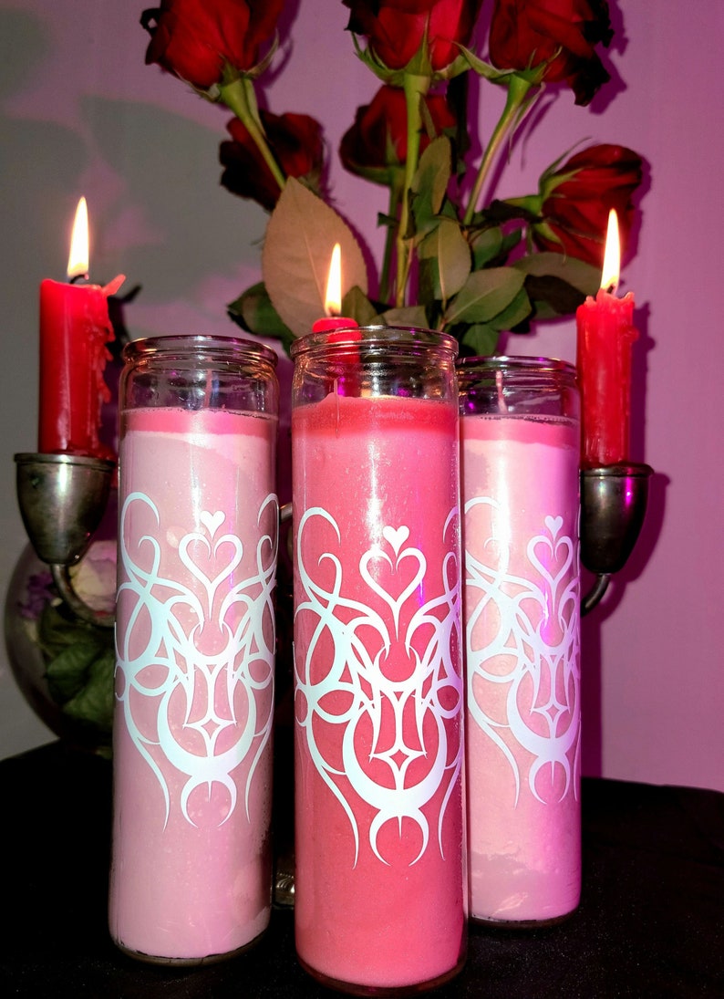 May include: Three pink and red glass candles with white decorative designs. The candles are in glass holders and are lit.