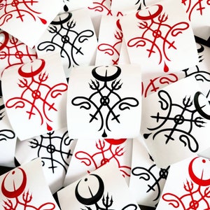 May include: A close-up of a pile of stickers featuring a black and red design with a crescent moon and trident. The stickers are printed on white paper.